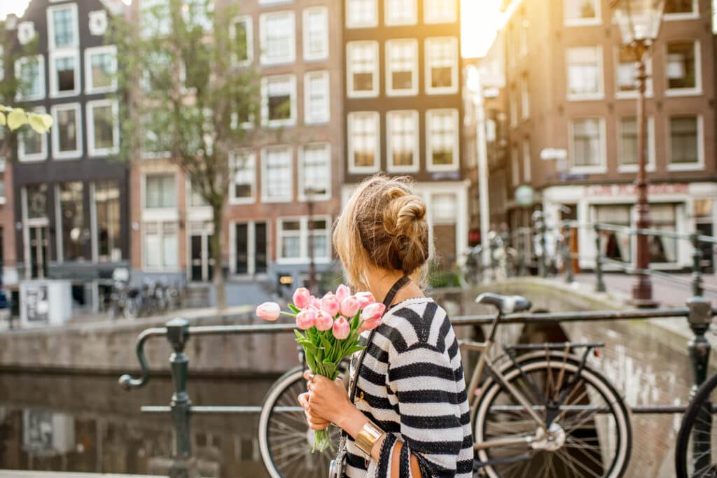 Lifestyle portrait of a woman walking with bouquet of pink tulips near the water channel in Amsterdam city