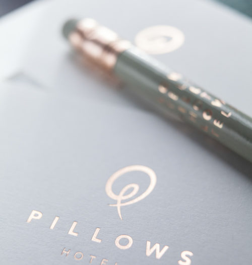 The logo of Pillows Hotels on a journal with a pencil