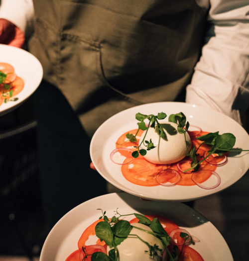 A waiter with three plates with tomato and mozzarella