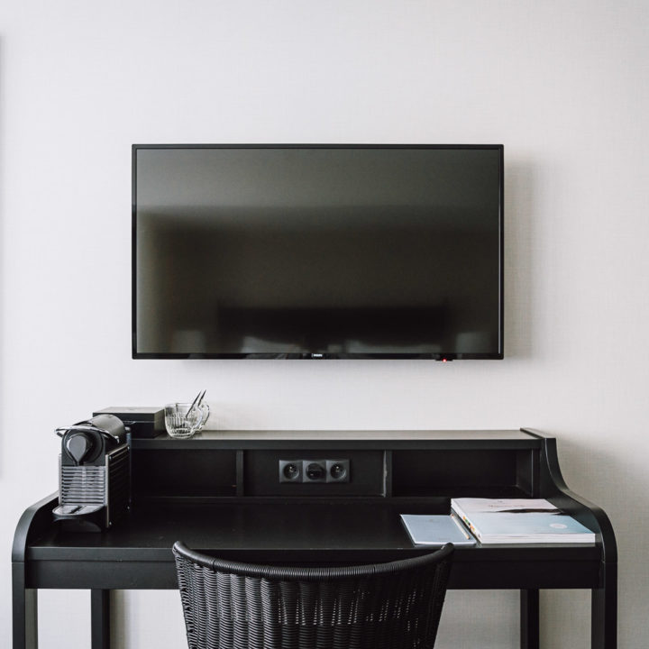 A flat screen tv above a black desk with a black chair