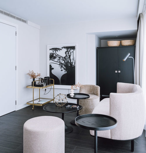 A bright hotel room with grey chairs with three small black round tables