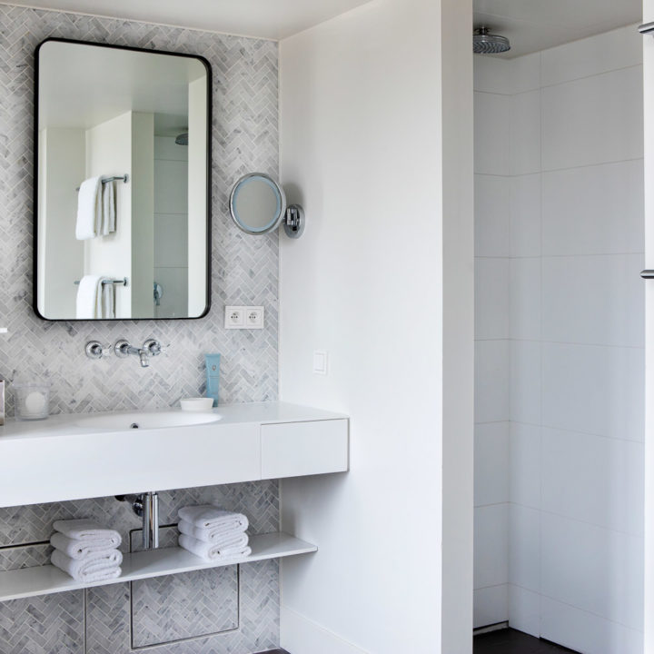 A hotel bathroom with grey tiles and a square mirror